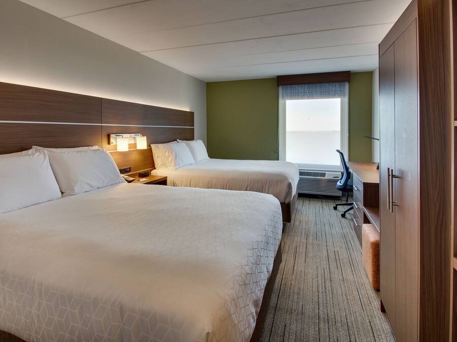 A hotel room with two beds, a desk, a chair, a lamp, and a window with blinds.