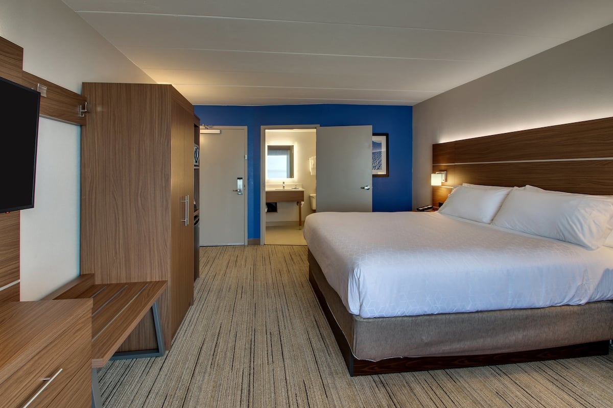 Een hotelkamer met een groot bed, een houten garderobe en een zichtbare badkamer door een geopende deur.