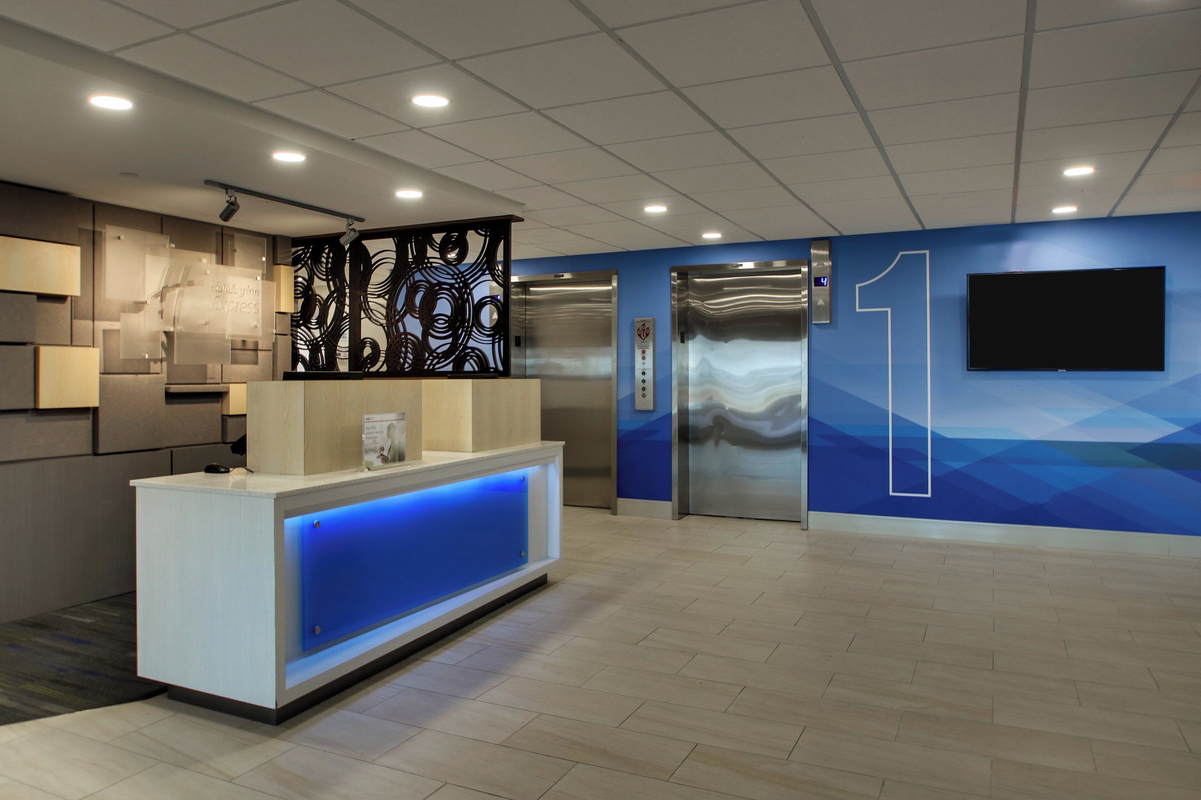 A modern reception area with a reception desk, a digital elevator display, and a large wall-mounted television.
