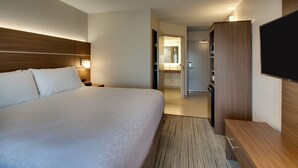 A hotel room with a large bed, a wooden headboard, a flat-screen TV, a wooden wardrobe, and a bathroom visible through an open door.