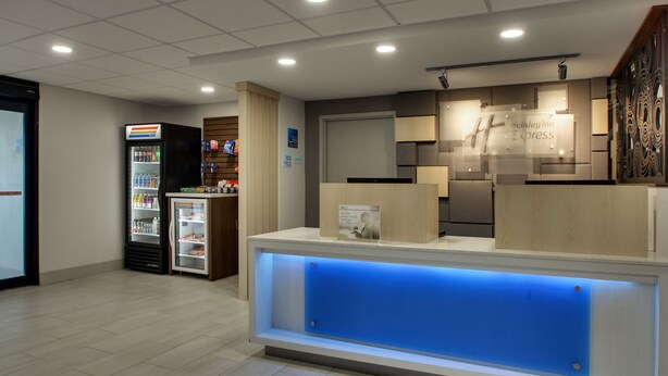 A hotel reception area with a reception desk, a refrigerator with beverages, and a wall-mounted sign for the Holiday Inn Express.