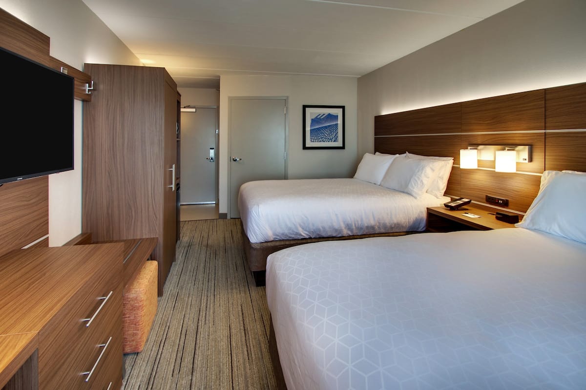 Een hotelkamer met twee bedden, een televisie, houten meubels en een ingelijst schilderij aan de muur.