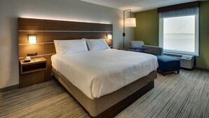 A hotel room with a large bed, bedside tables, a lamp, a chair, and a window with blinds.