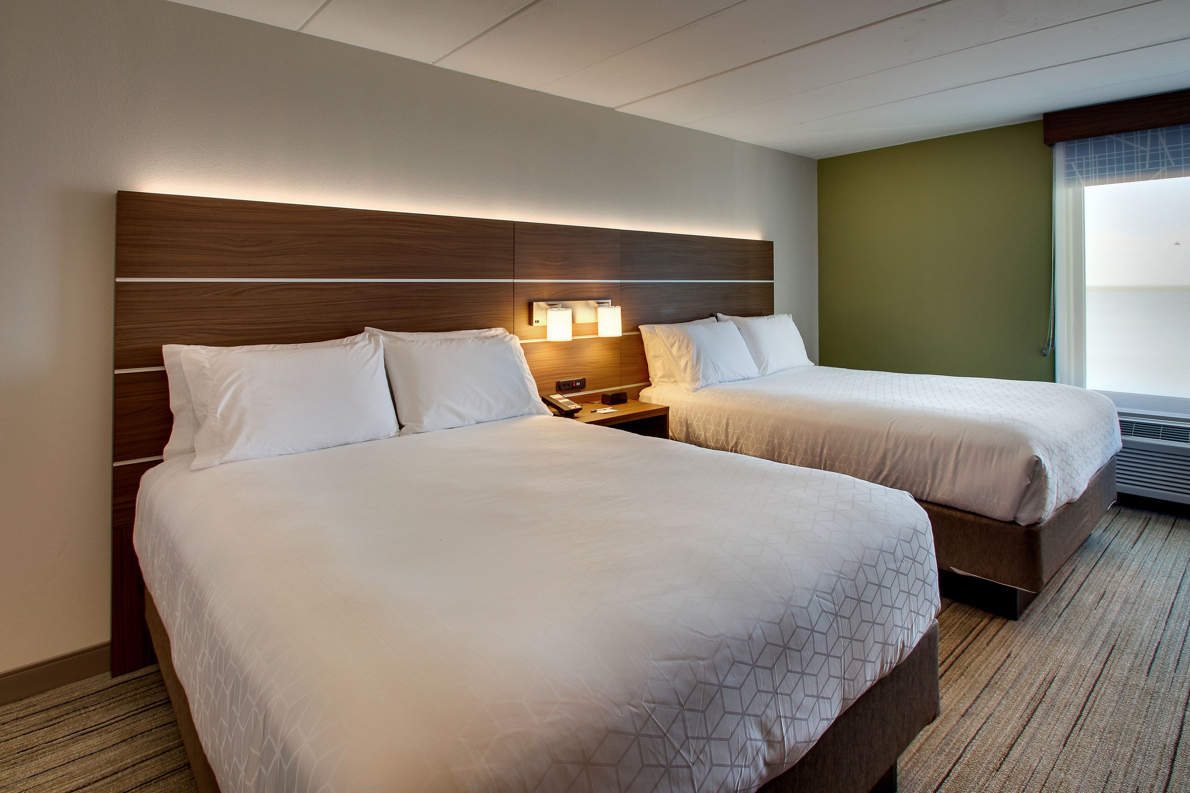 Een hotelkamer met twee bedden, een houten hoofdbord, nachtlampjes en uitzicht op de omgeving.