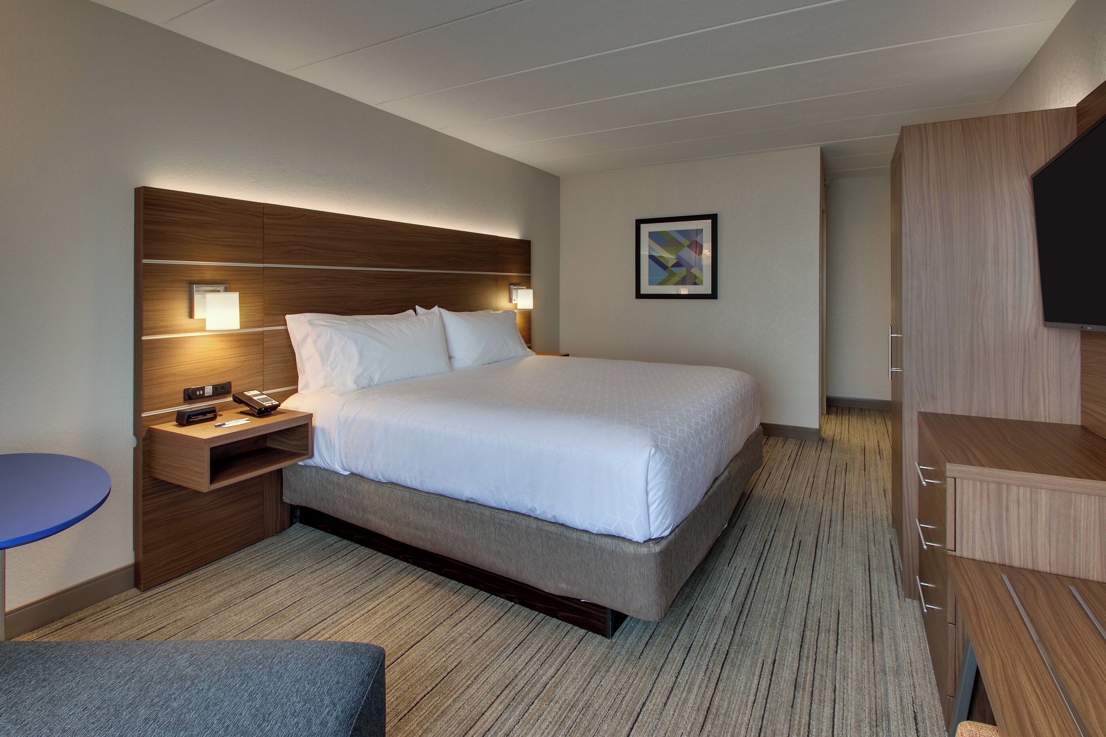 Una camera d'albergo con un letto grande, un comodino con telefono e lampada, un tavolino piccolo e una TV su un mobile in legno.