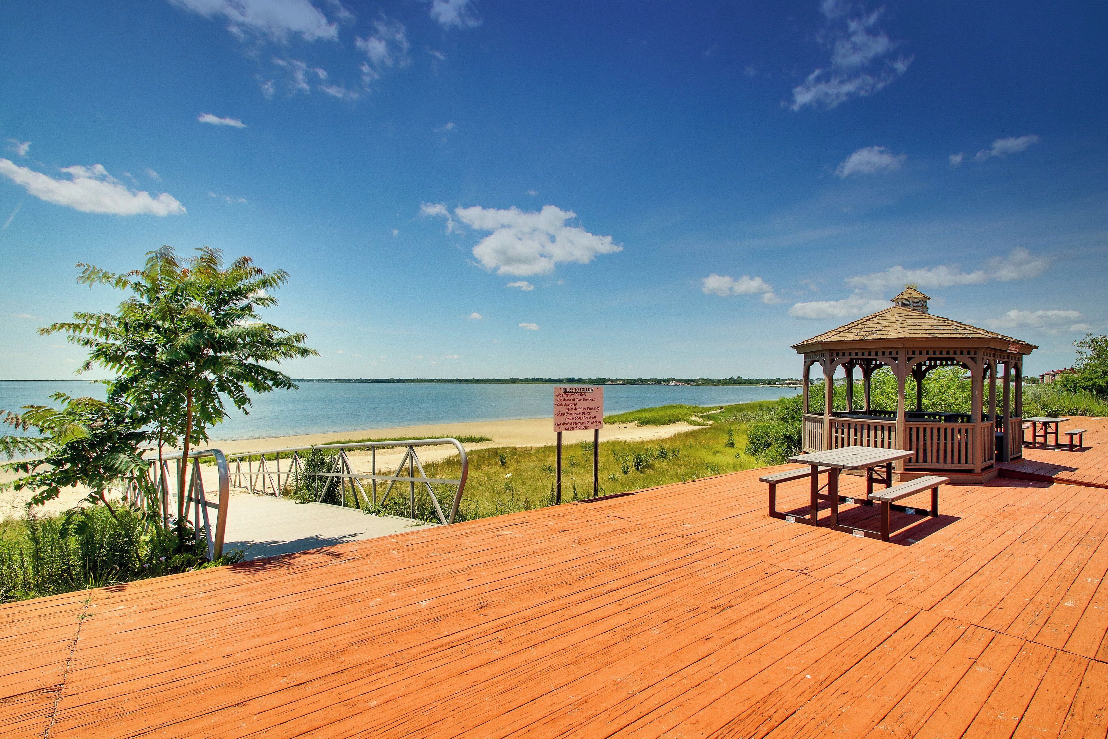 Una terraza de madera con un mirador, mesas de picnic y vista al mar.