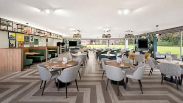 A spacious indoor dining area with multiple seating options, including booths and tables, and a large window offering a view of the outdoors.