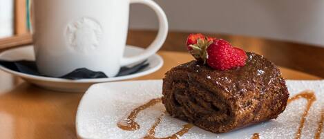 Un postre con fresa encima, una taza de café y azúcar glas en un plato.