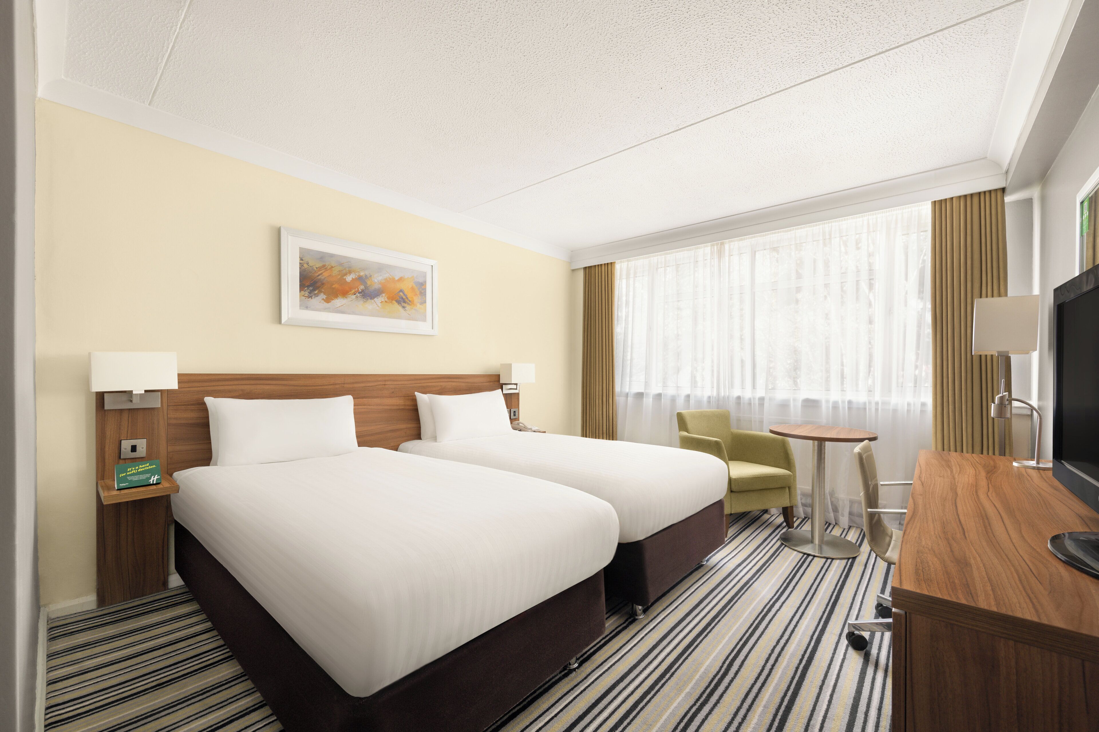 A hotel room with two beds, a desk, a chair, a television, and a window with curtains.