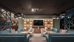 A modern living room with a large flat-screen TV, two armchairs, a sofa, and a coffee table. There are shelves with decorative items and a bookshelf in the background. - Holiday Inn York by IHG (York)