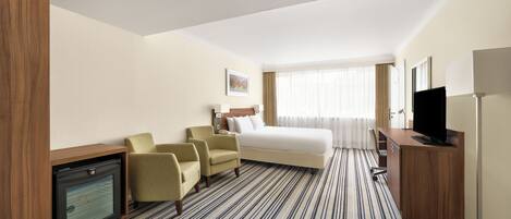 Habitación de hotel con una cama, dos sillones, un escritorio con televisor y un minibar.