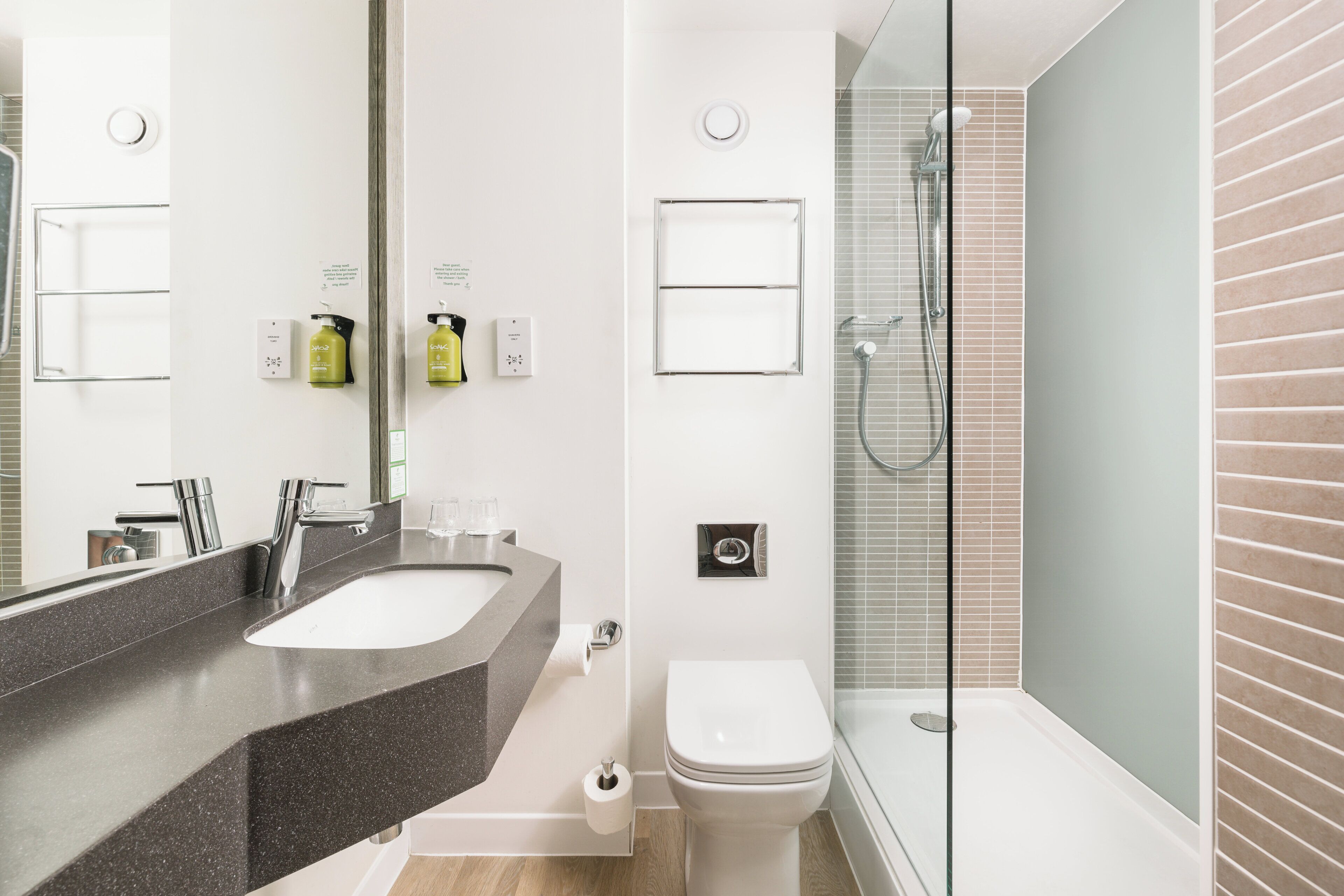 Un baño moderno con un espejo grande, un lavamanos, un inodoro y una zona de ducha con paredes de vidrio.