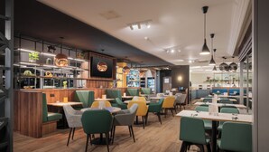 A modern restaurant with wooden accents, green and yellow chairs, and pendant lighting. - Holiday Inn York by IHG (York)