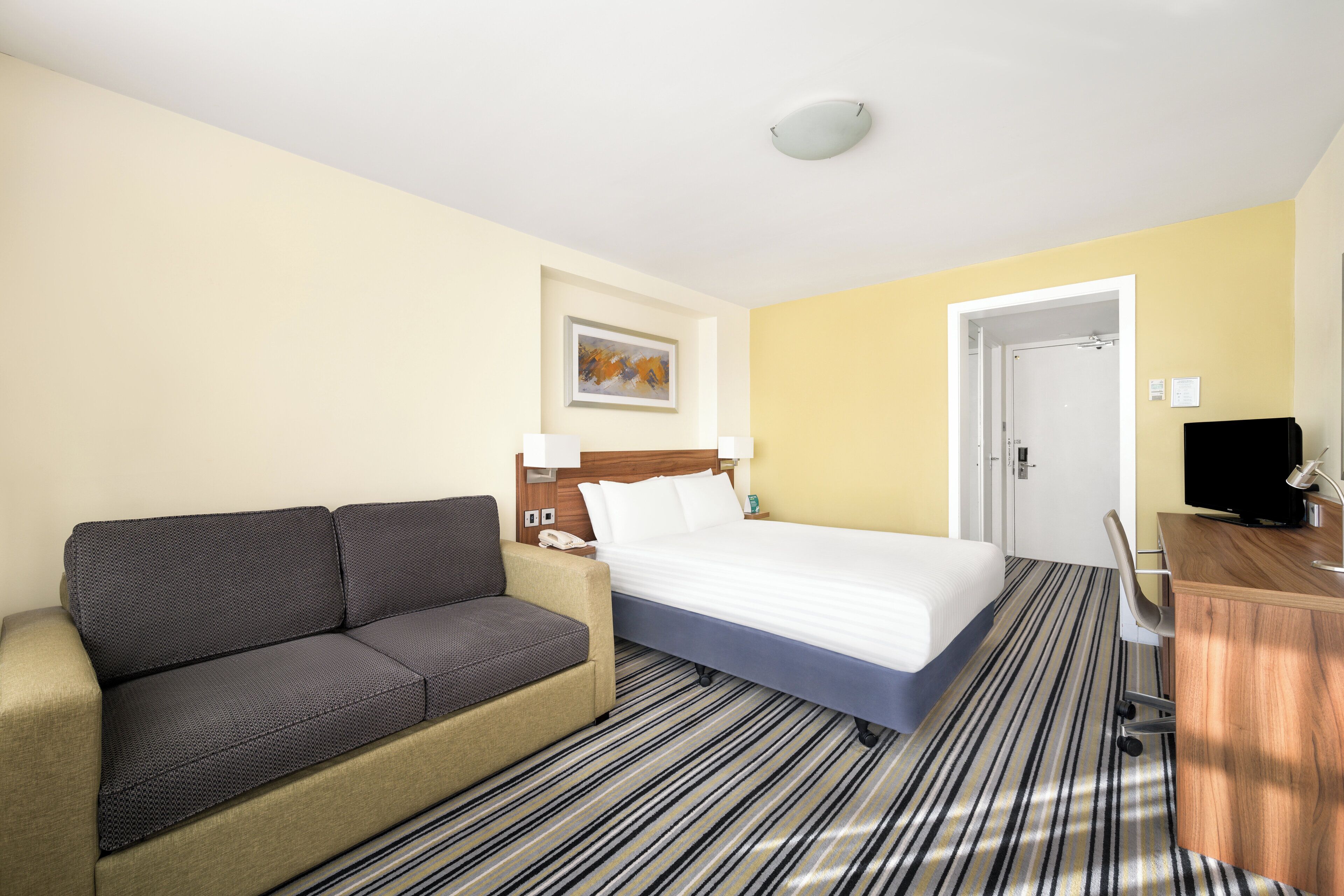 A hotel room with a bed, a sofa, a desk, and a television.