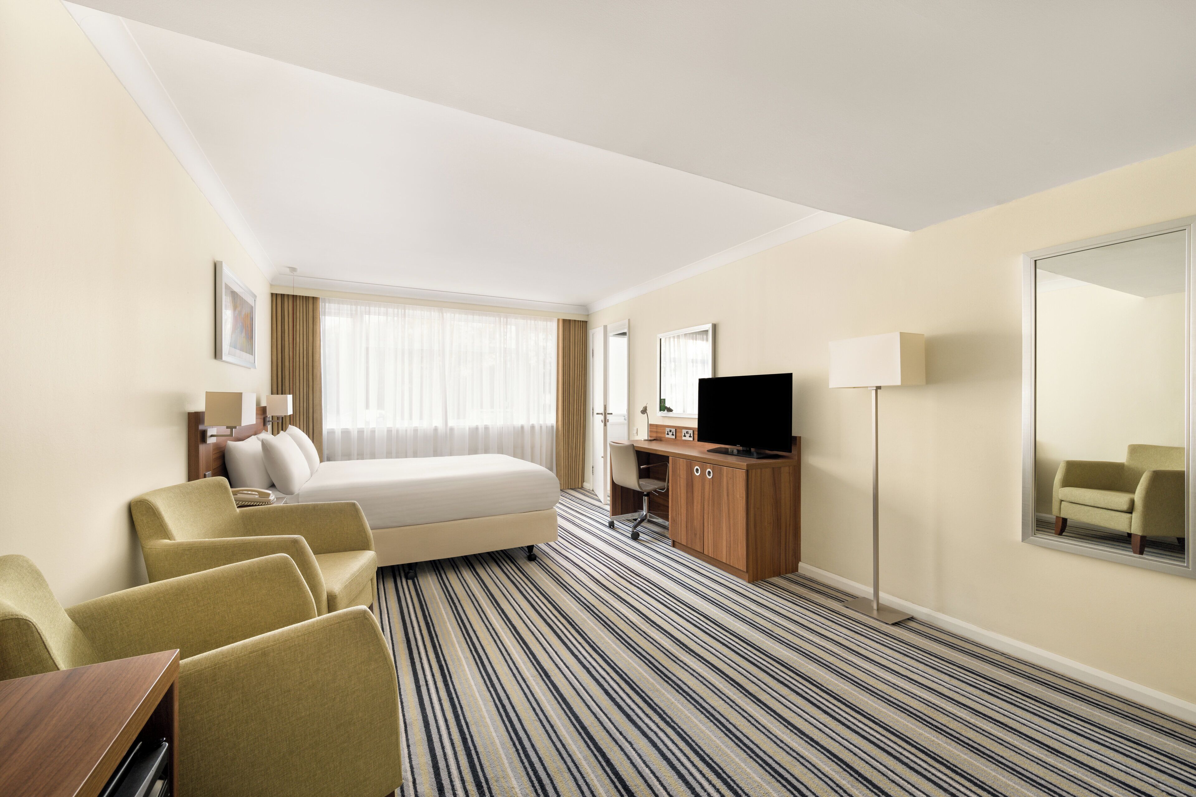 A hotel room with a bed, a desk, a television, and a mirror.
