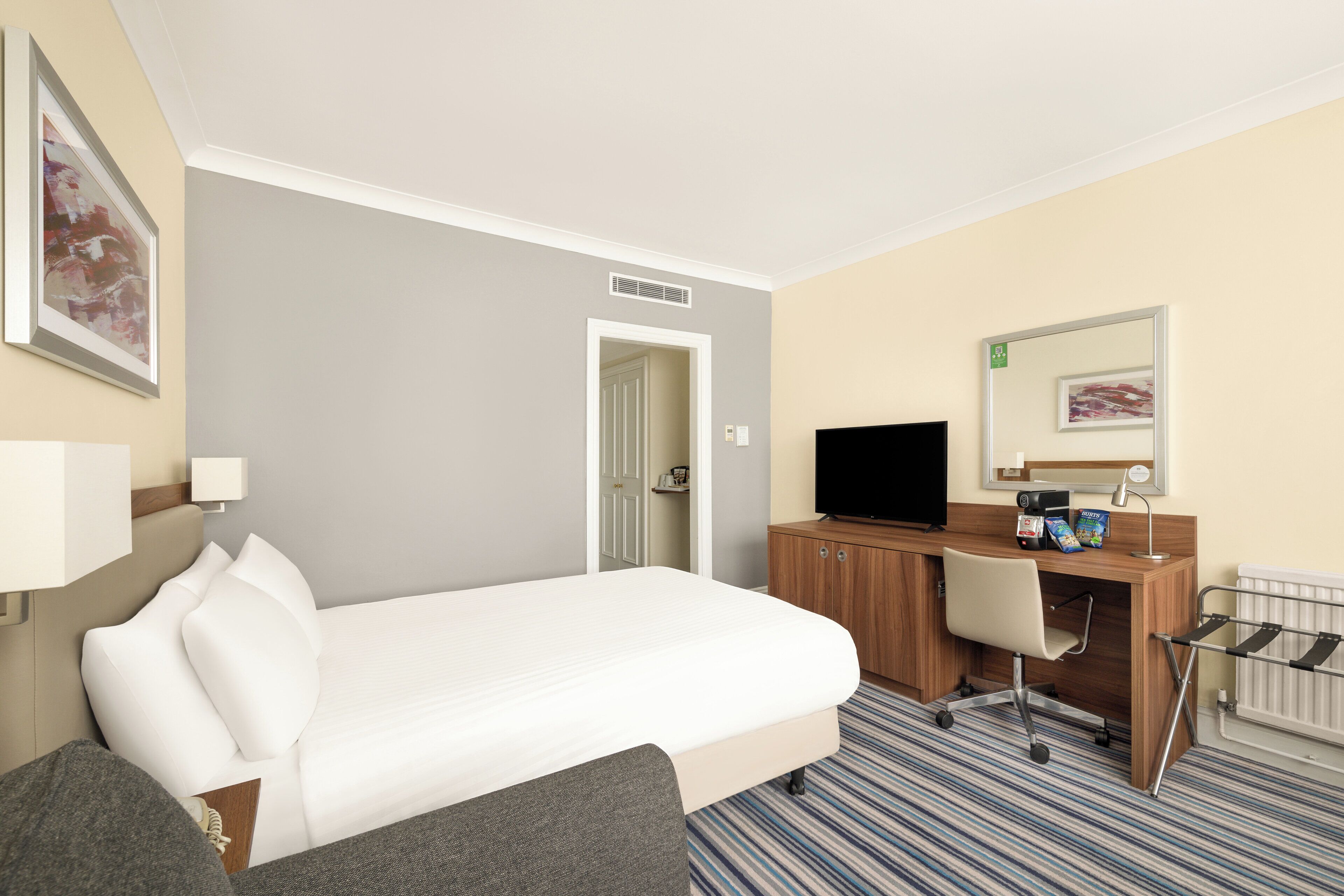 Ein Hotelzimmer mit einem Bett, einem Schreibtisch mit Computer, einem Sessel, einem Fernseher und einer Heizung.