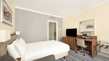 A hotel room with a bed, a desk with a computer, a chair, a television, and a radiator.