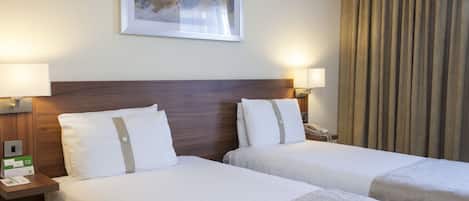 Une chambre d’hôtel avec deux lits, une tête de lit en bois, une œuvre d’art encadrée au mur et un rideau à la fenêtre.