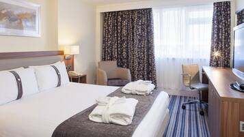 Habitación de hotel con una cama grande, un escritorio con computadora, una silla y un televisor.