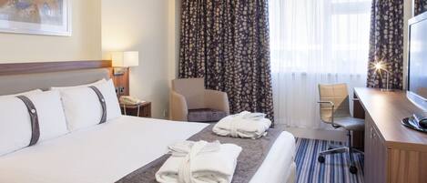 A hotel room with a large bed, a desk with a computer, a chair, and a TV.