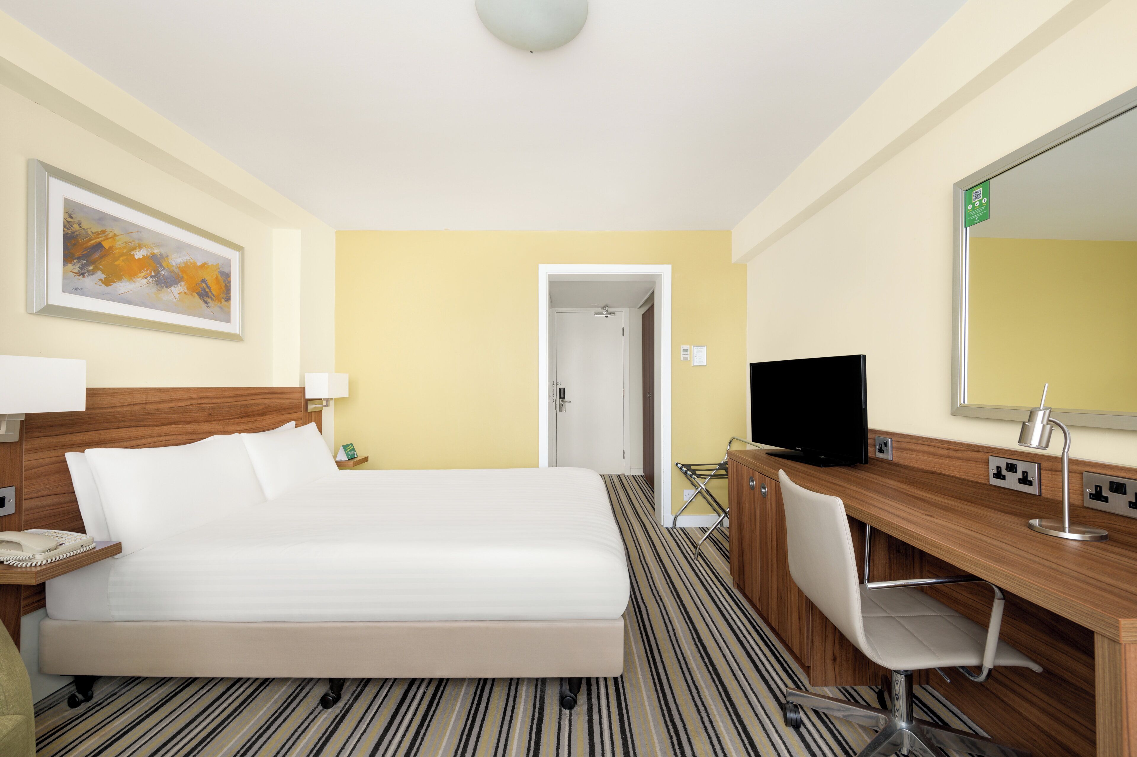 A hotel room with a bed, a desk with a chair, a television, and a mirror.