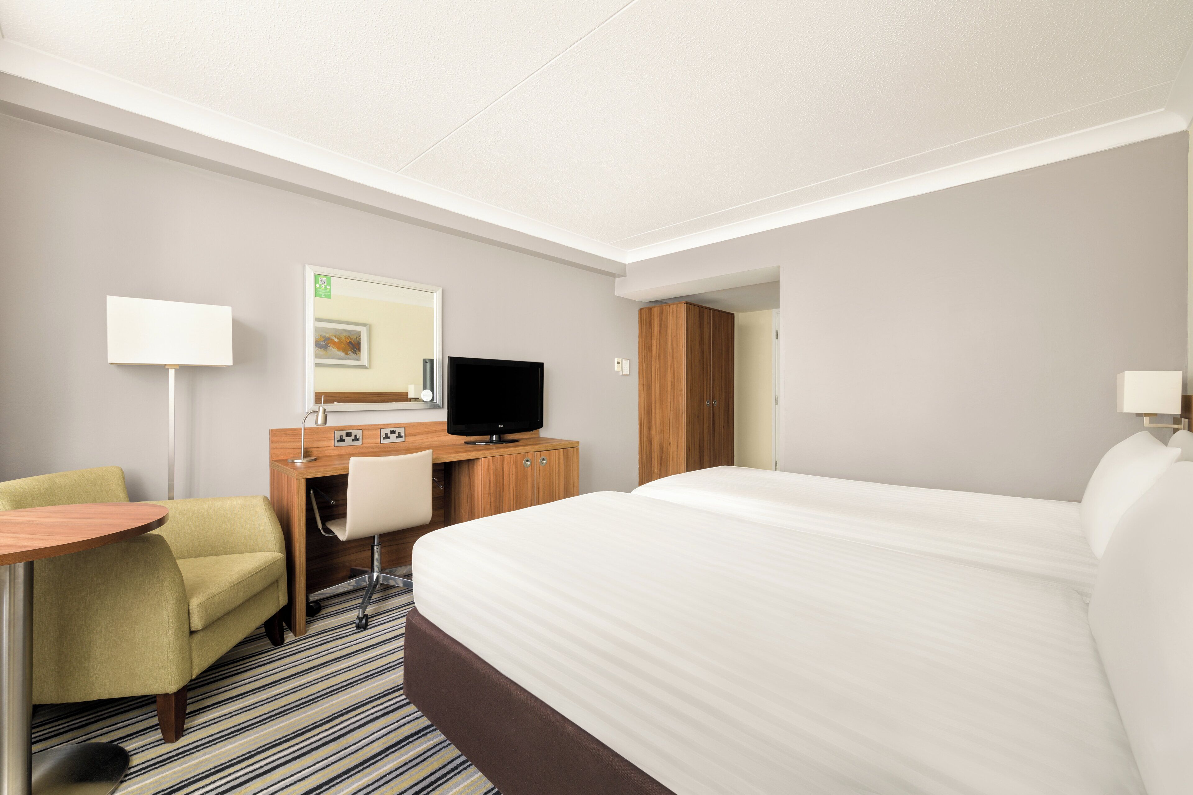 A hotel room with a bed, a desk, a chair, a TV, and a lamp.
