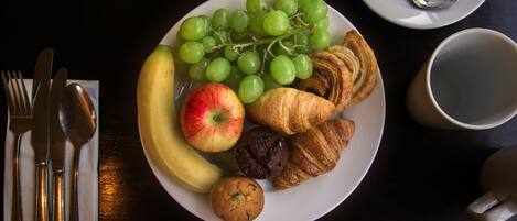 Un plato con plátano, manzana, uvas, croissants y un muffin.