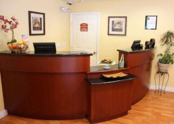 A reception area with a wooden desk, a computer, framed pictures on the wall, and a door with a sign.