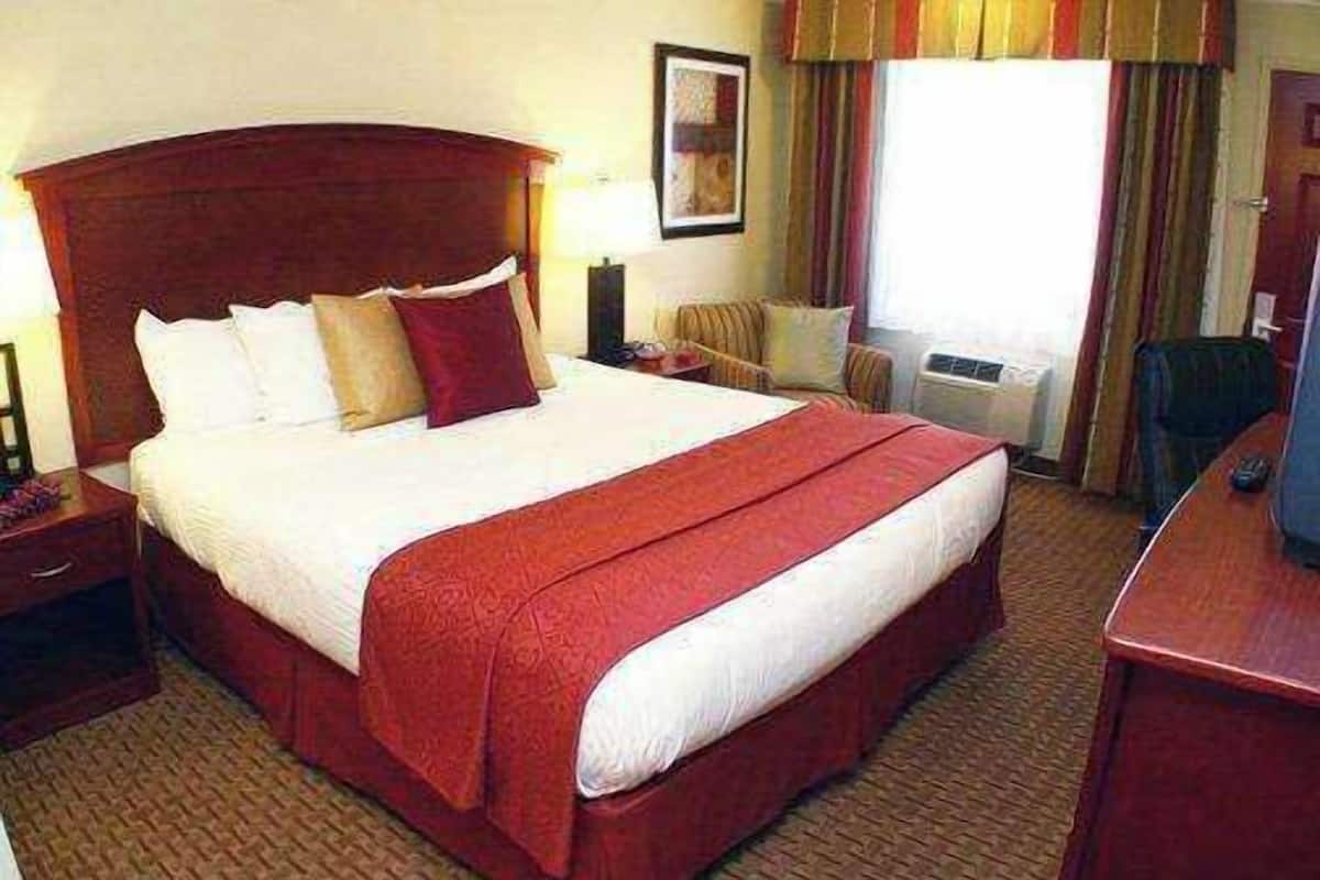 A hotel room with a large bed, a wooden headboard, a desk, and a chair.