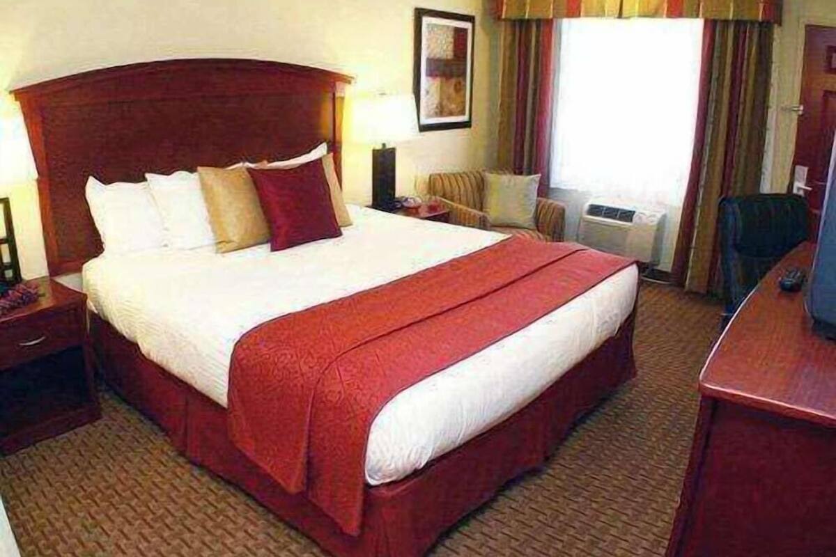 A hotel room with a large bed, a desk, a chair, and a window with curtains.