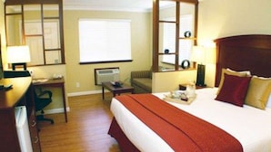 Ein Hotelzimmer mit einem großen Bett, einem Schreibtisch, einem Sessel, einem kleinen Tisch, einem Spiegel und einem Fenster.