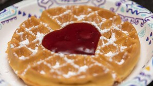 Uma waffle com recheio em formato de coração e açúcar de confeiteiro em um prato estampado.