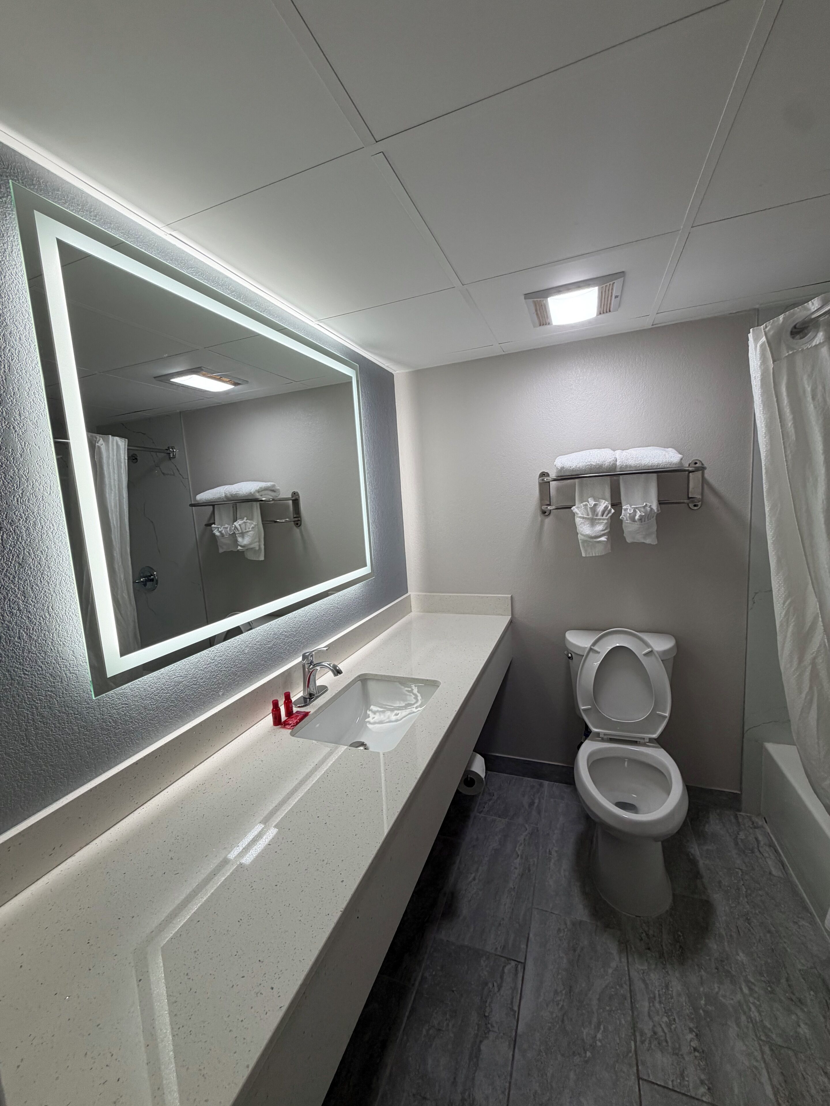 Un baño moderno con un espejo grande, un lavamanos, un inodoro y una cortina de ducha.