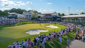 Um campo de golfe com espectadores, um clube e uma grande estrutura de tenda.