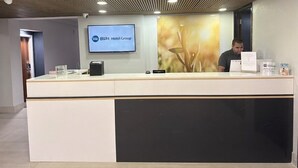 Un comptoir d’accueil doté d’un écran numérique affichant le nom du groupe hôtelier, un homme assis derrière, et un design moderne au niveau du plafond.