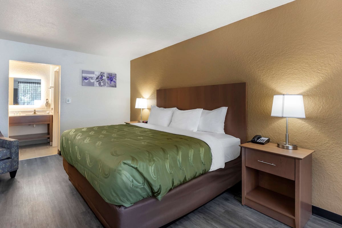 Ein Hotelzimmer mit einem großen Bett, zwei Nachttischlampen, einem Holznachttisch und einem Schreibtisch mit Stuhl.