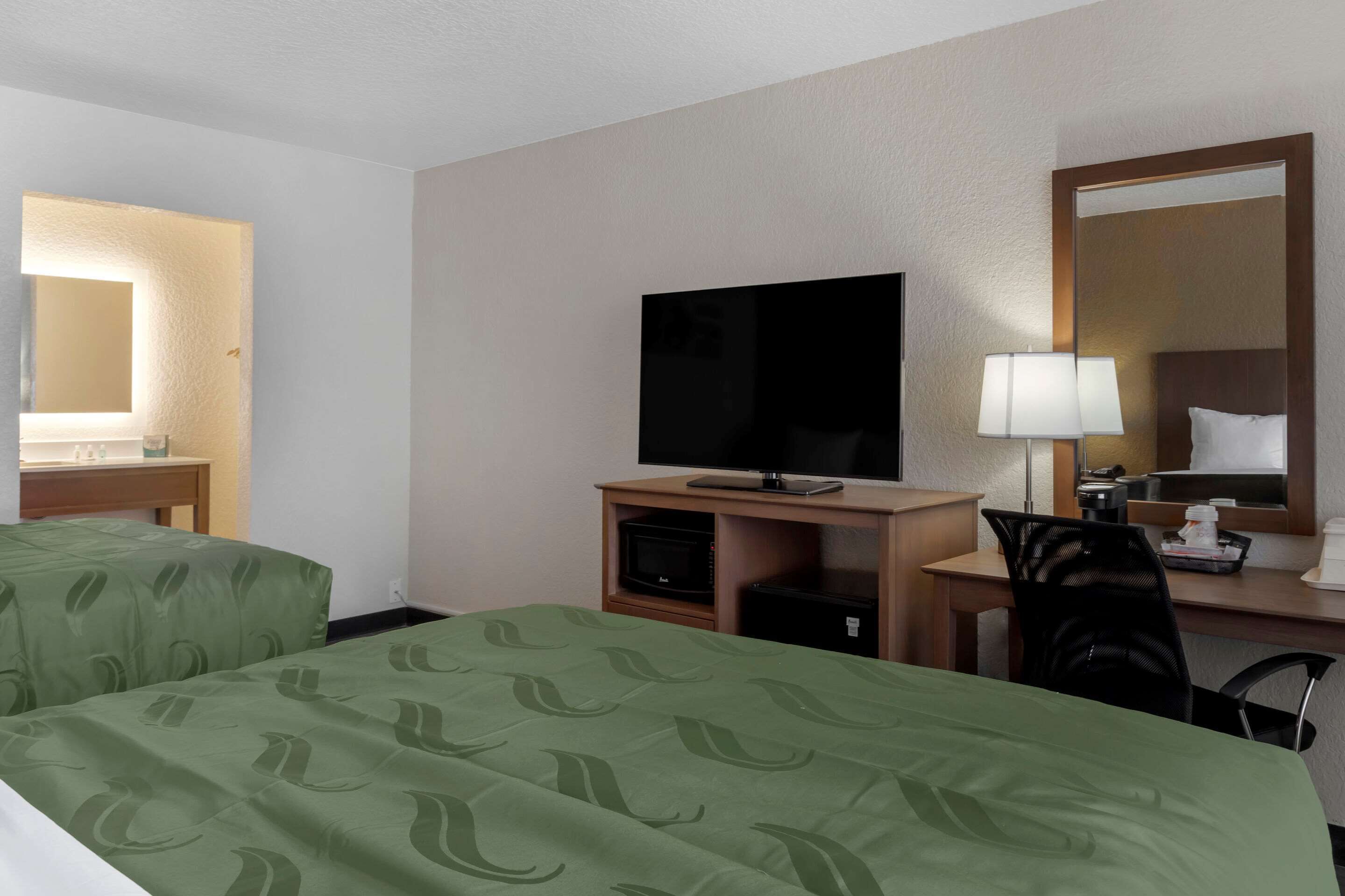 Une chambre d’hôtel avec deux lits, un bureau équipé d’une télévision, d’une lampe et d’un miroir.