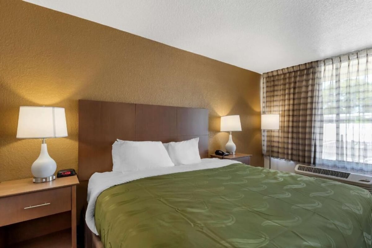 A hotel room with a bed, two bedside tables with lamps, a telephone, and a window with curtains.