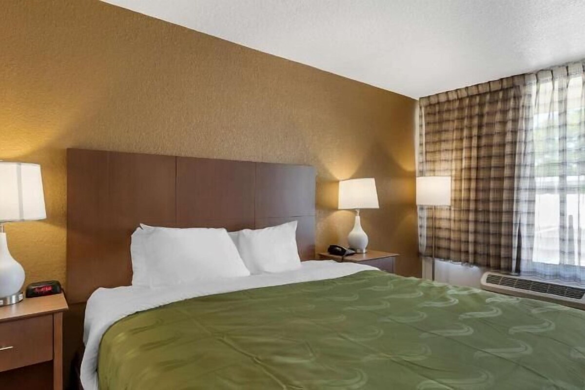 A hotel room with a bed, two bedside tables with lamps, a window with curtains, and a wall with a textured pattern.