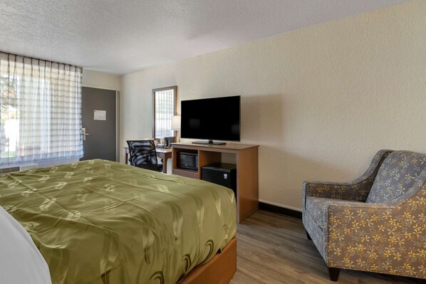 A hotel room with a bed, a desk with a television, a chair, and a window with curtains.