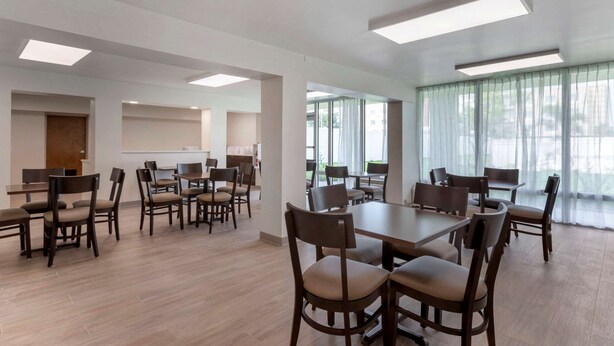 Uma sala de conferências ampla, com várias mesas e cadeiras, janelas grandes com cortinas leves e iluminação embutida no teto.