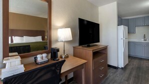 Quarto de hotel com escrivaninha de madeira, espelho, televisão, máquina de café, frigorífico e kitchenette.