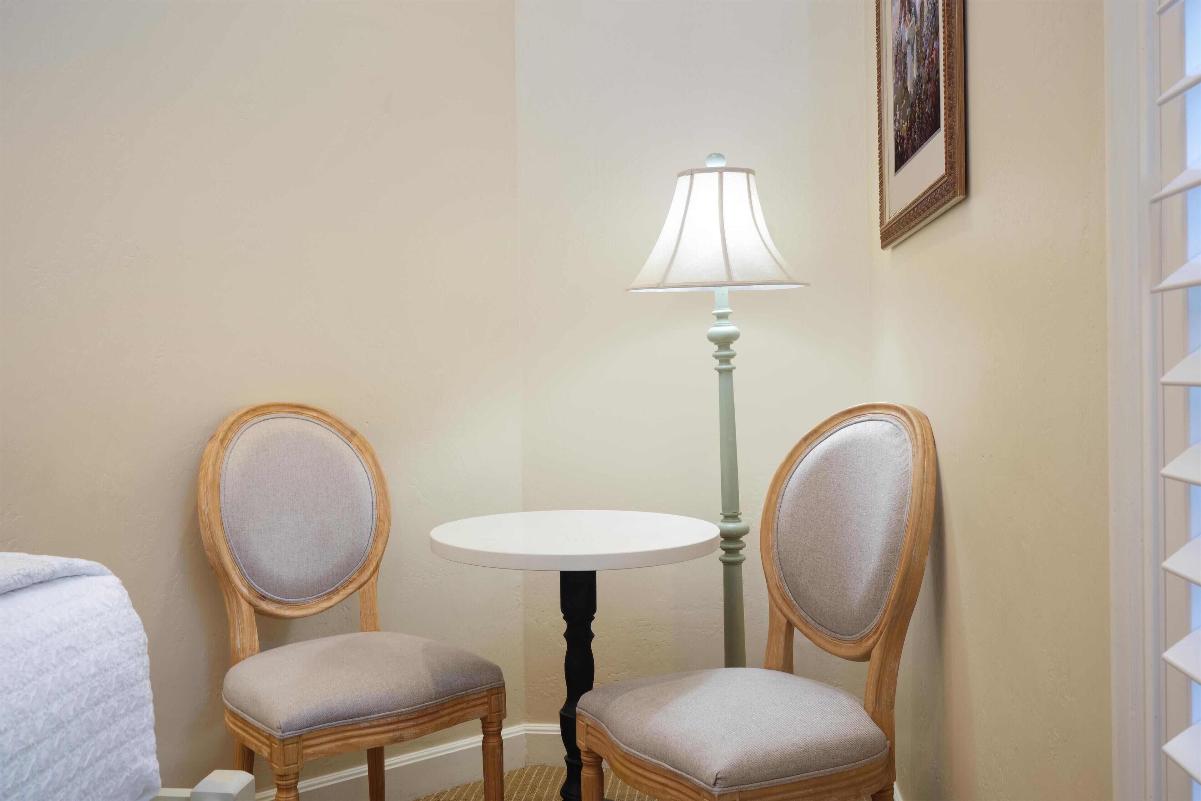 Ein Eckzimmer mit zwei Polstersesseln, einem kleinen runden Tisch, einer Lampe und einem gerahmten Bild an der Wand.