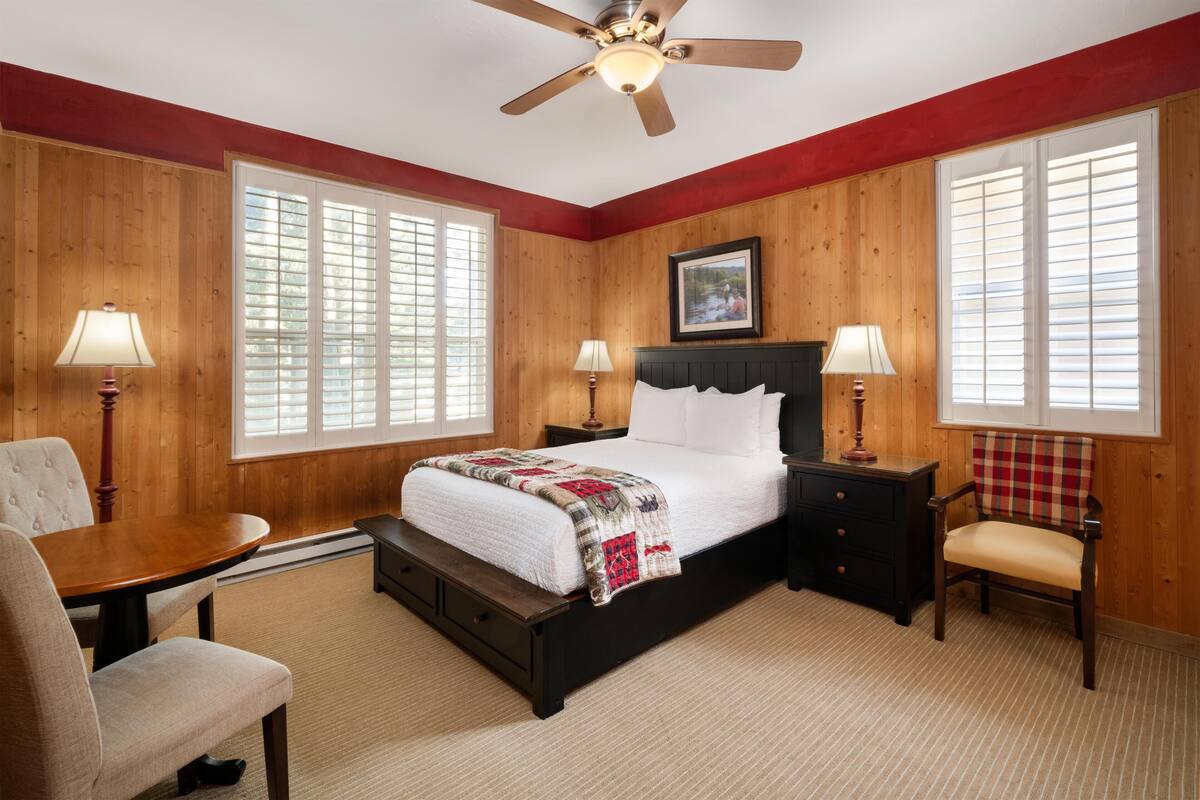 A bedroom with a bed, two nightstands, a chair, a table, and a ceiling fan.