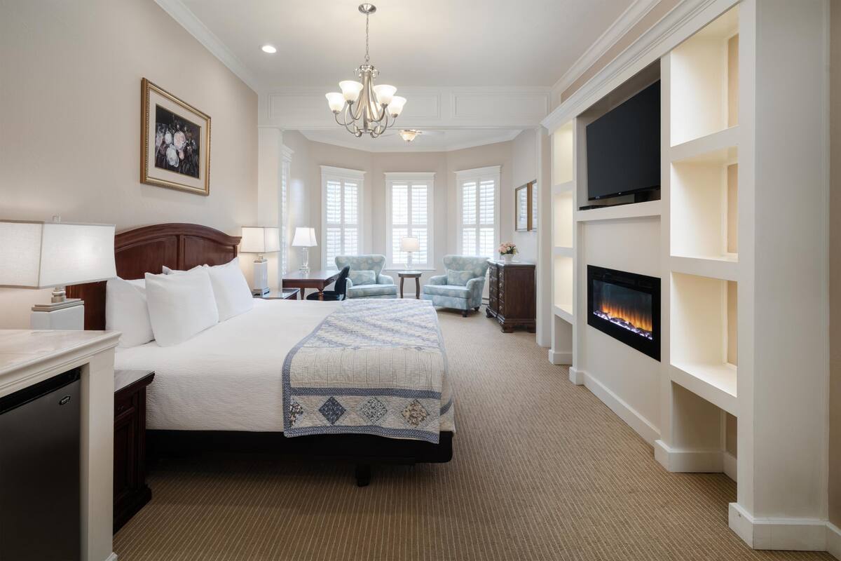 A hotel room with a large bed, a television, a fireplace, and a chandelier.