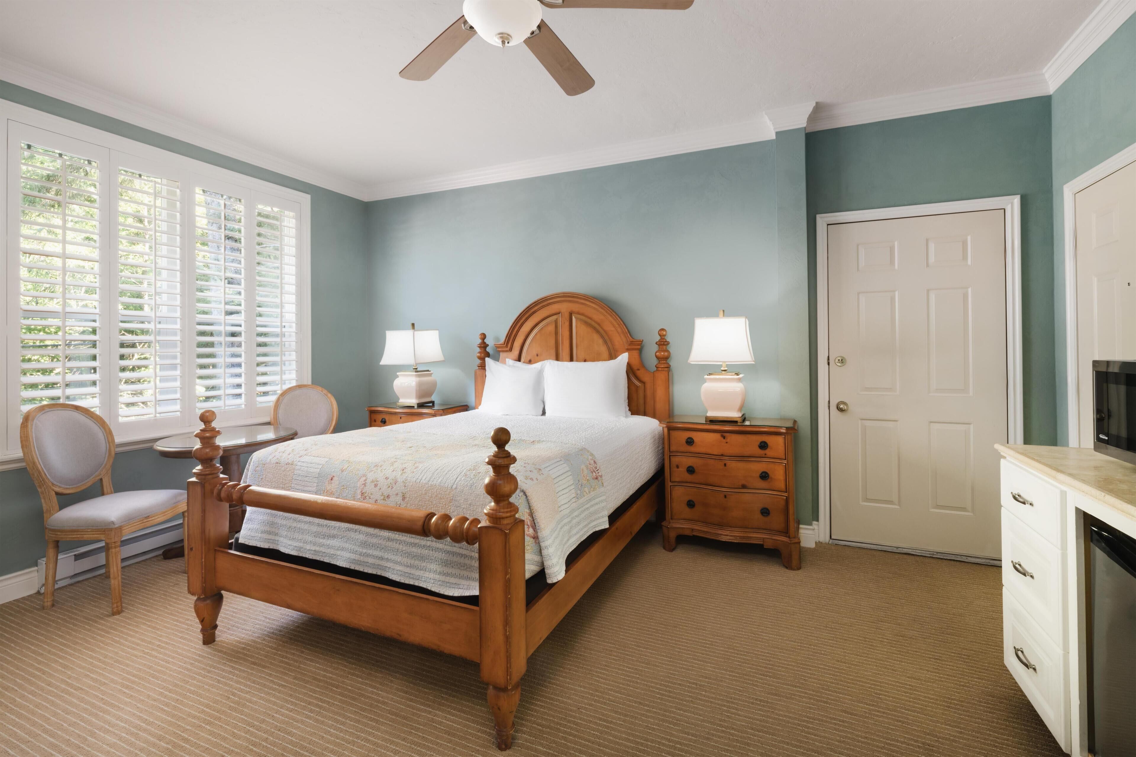 A bedroom with a wooden bed, two bedside tables with lamps, a chair, a wardrobe, and a door.