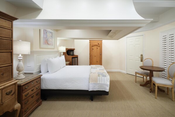 A bedroom with a bed, dresser, nightstand, lamp, and a small table with chairs.