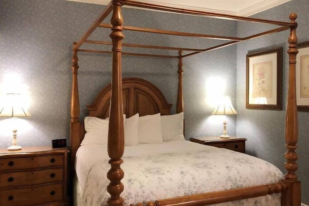 A four-poster bed with a wooden headboard, two bedside tables with lamps, and framed artwork on the walls.