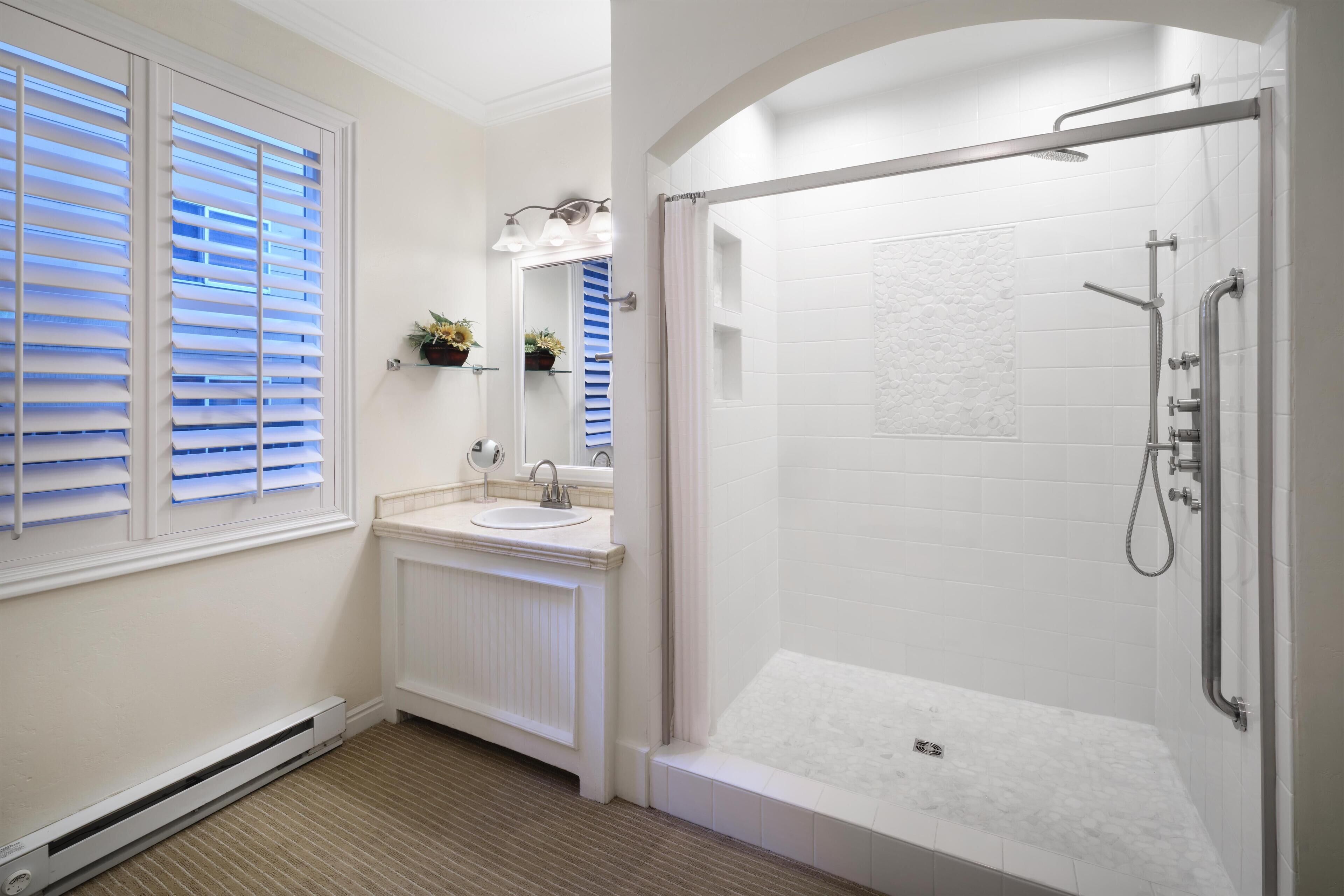 Ein Badezimmer mit begehbarer Dusche, Waschbecken und einem Fenster mit Jalousien.
