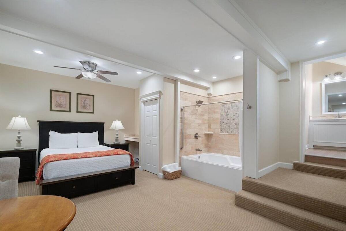 Habitación de hotel con cama, lámparas de noche, ventilador de techo, ducha y bañera.